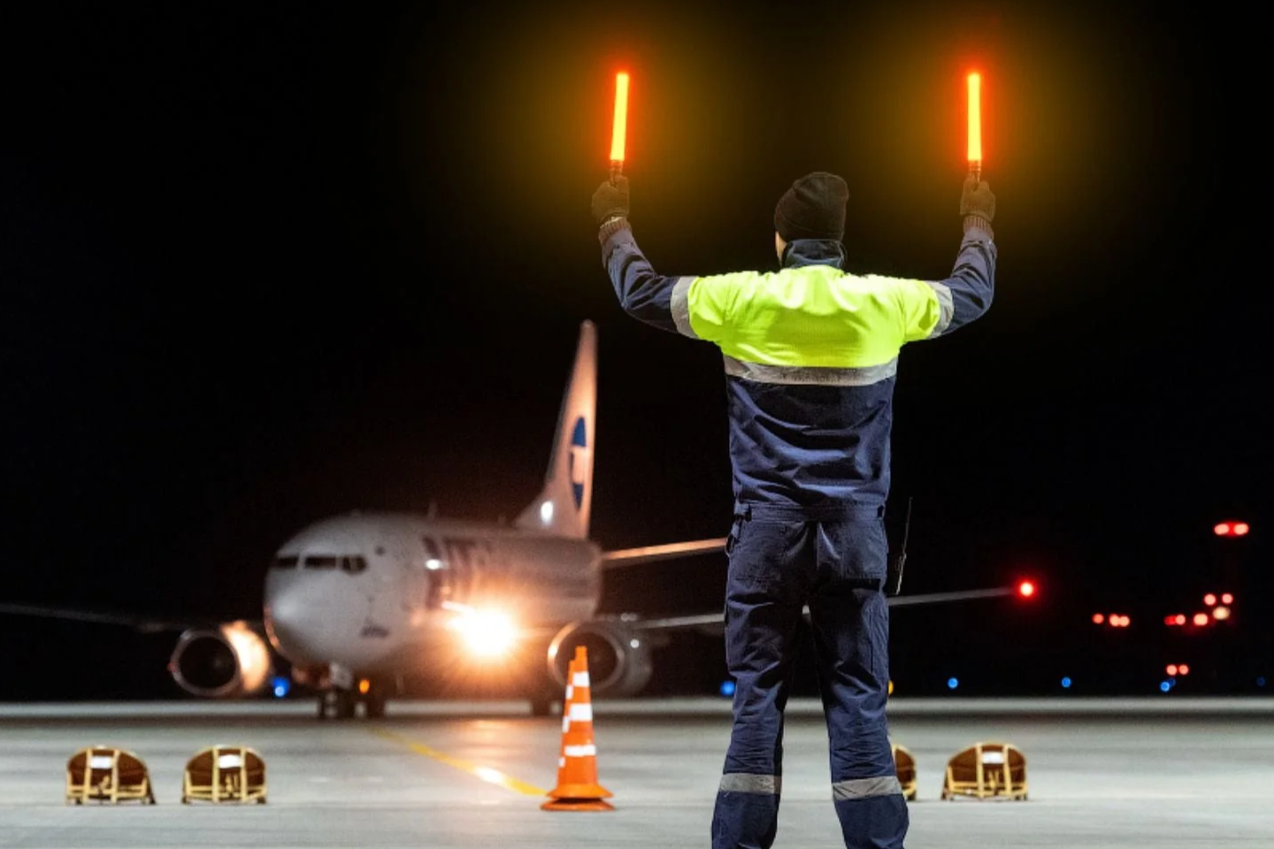 Airport ground crew with illuminated traffic wands guiding airplane at night